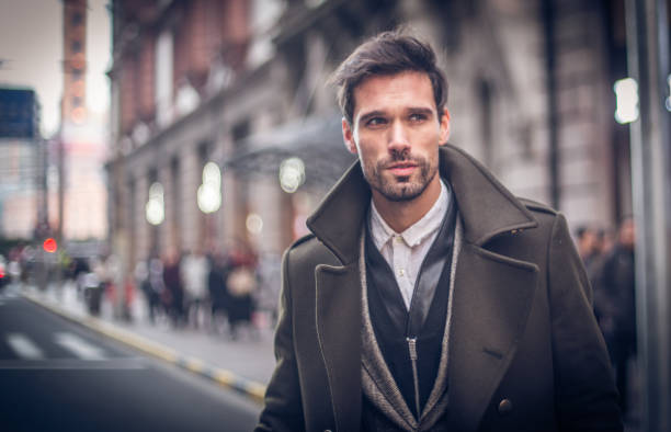 A stylish man in a modern coat walks down a city street, showcasing the latest fashion trends for men.